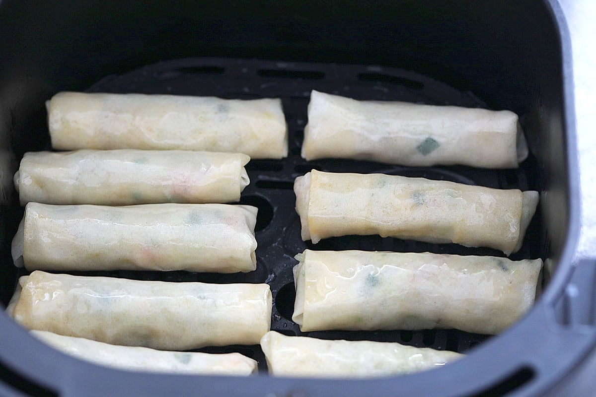 Raw spring rolls in air fryer basket.