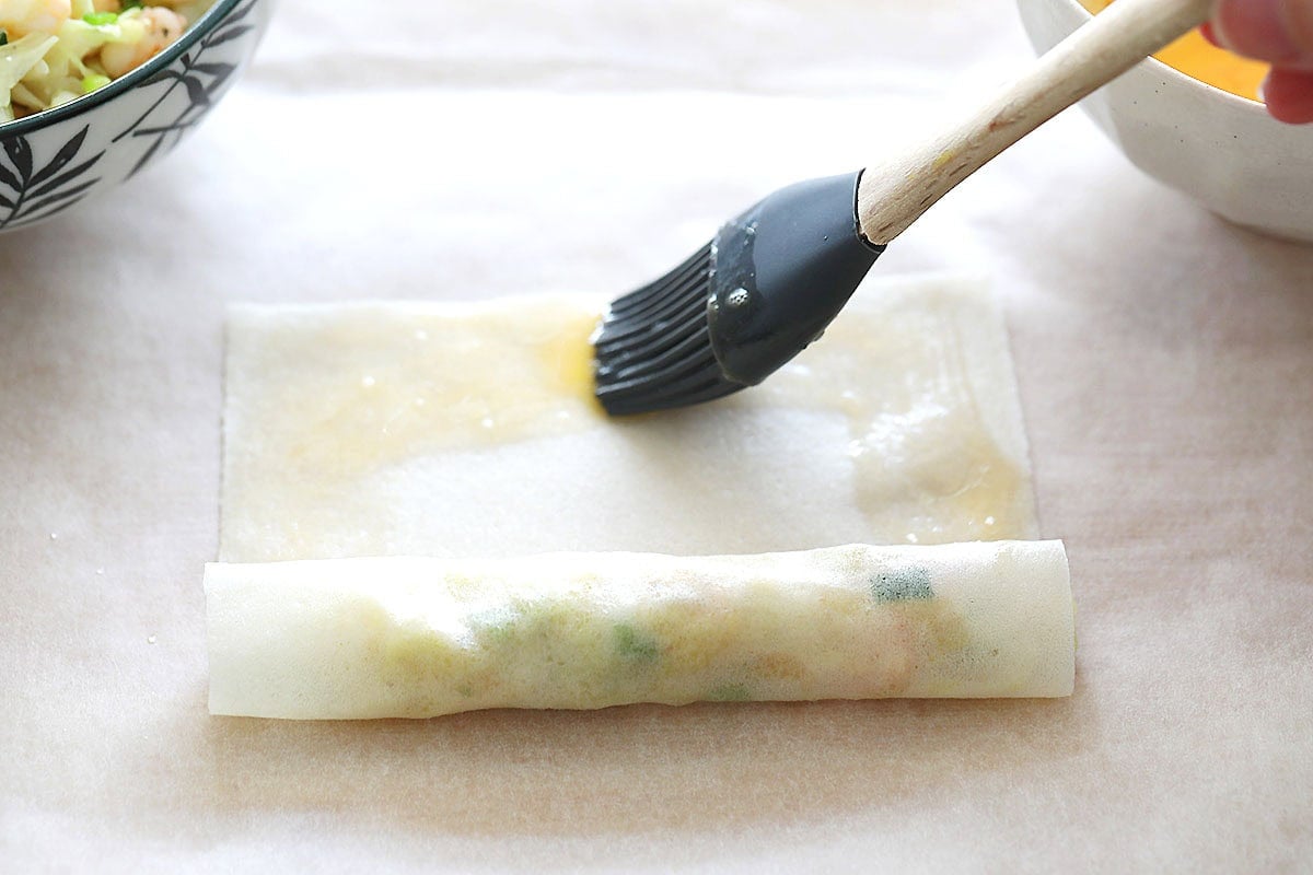 Brushing egg wash on spring roll wrapper edges.