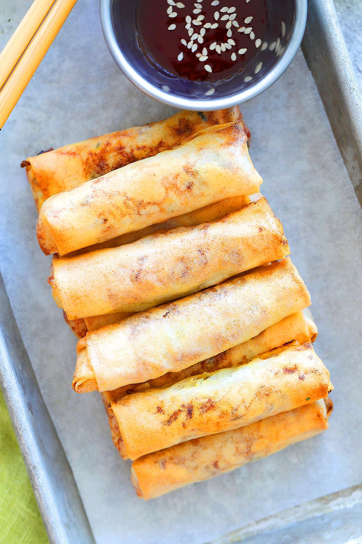 Golden crispy air fryer spring rolls with chili sauce on a tray.