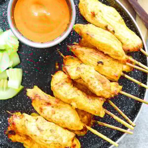 Juicy air fryer Thai chicken satay skewers with golden edges, served with fresh cucumber slices and homemade Thai peanut satay sauce.