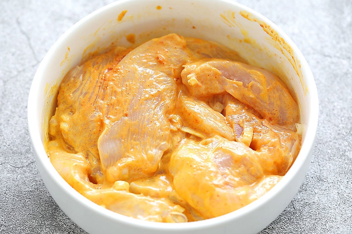 Chicken breast pieces mixed with lemongrass and spices in a bowl for satay marinade.