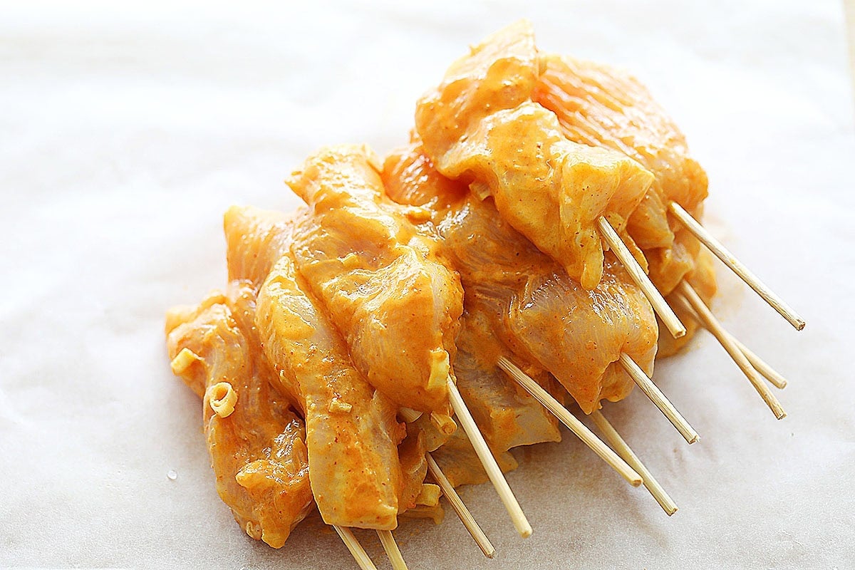 Raw Thai chicken satay skewers on a cutting board with parchment paper.