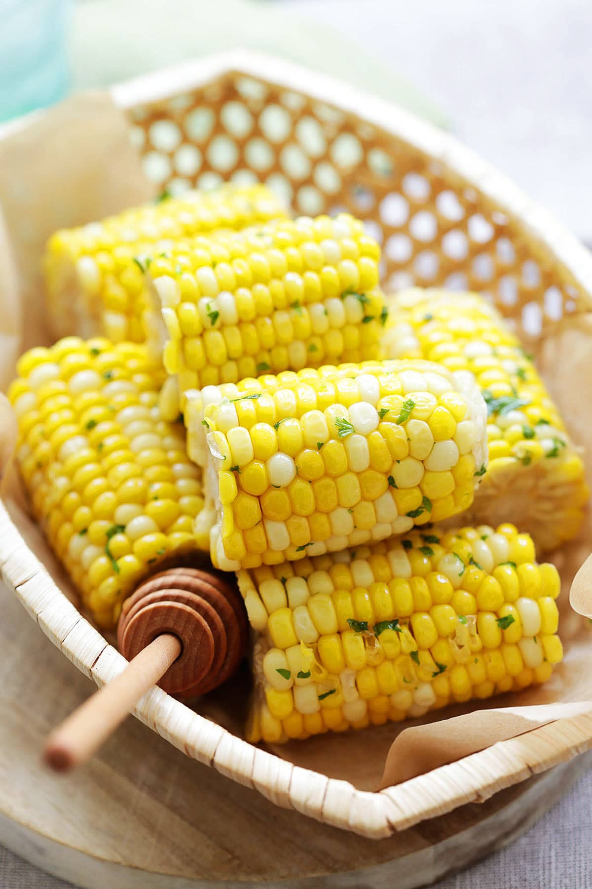 Honey butter corn on the cob served in a wooden basket with chopped parsley.