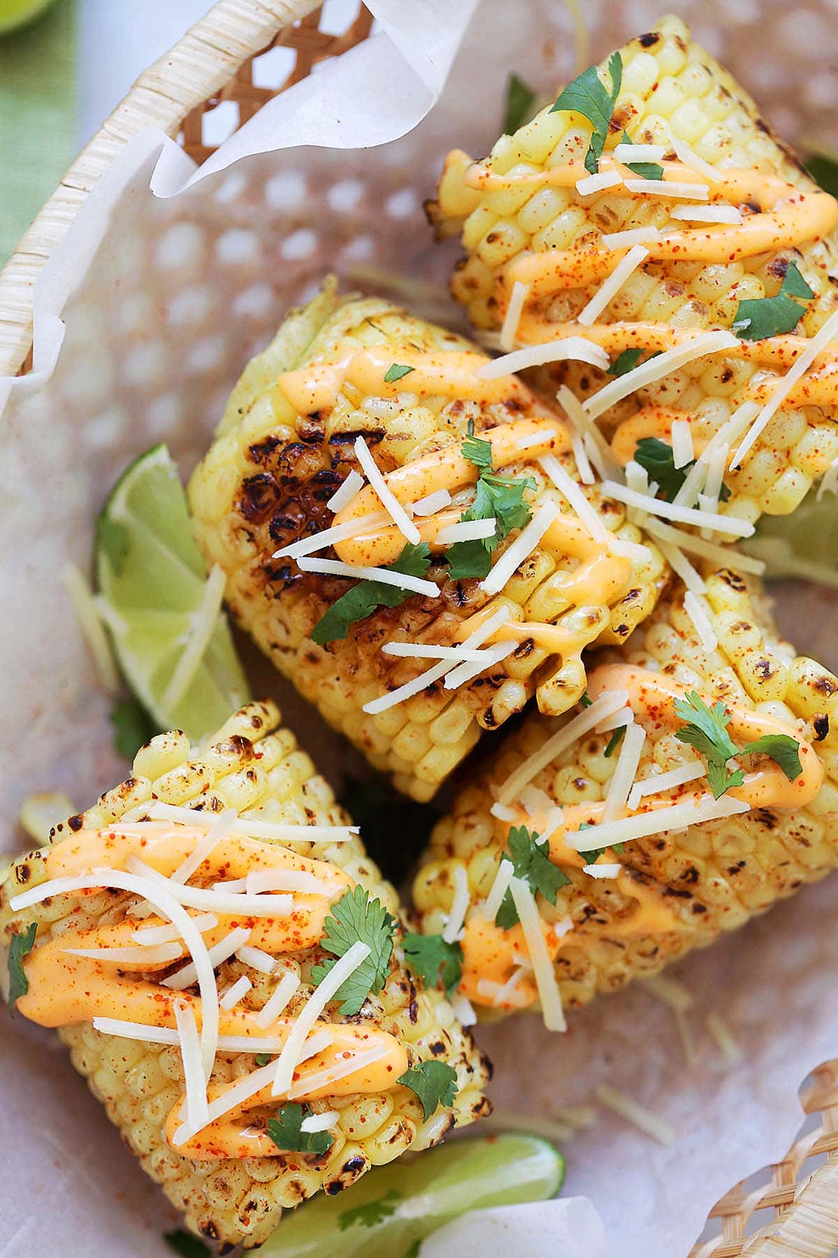 Grilled elote served in a basket, topped with Parmesan cheese.