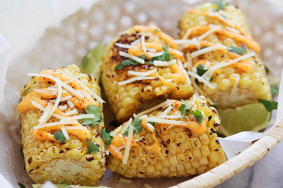 Mexican-style grilled corn on the cob served with lime wedges in a basket.