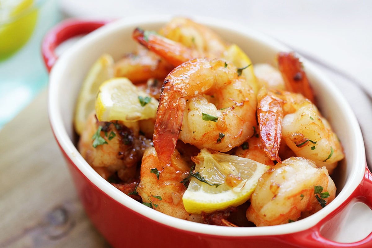 Oven baked shrimp with garlic butter in a serving dish with lemon wedges.