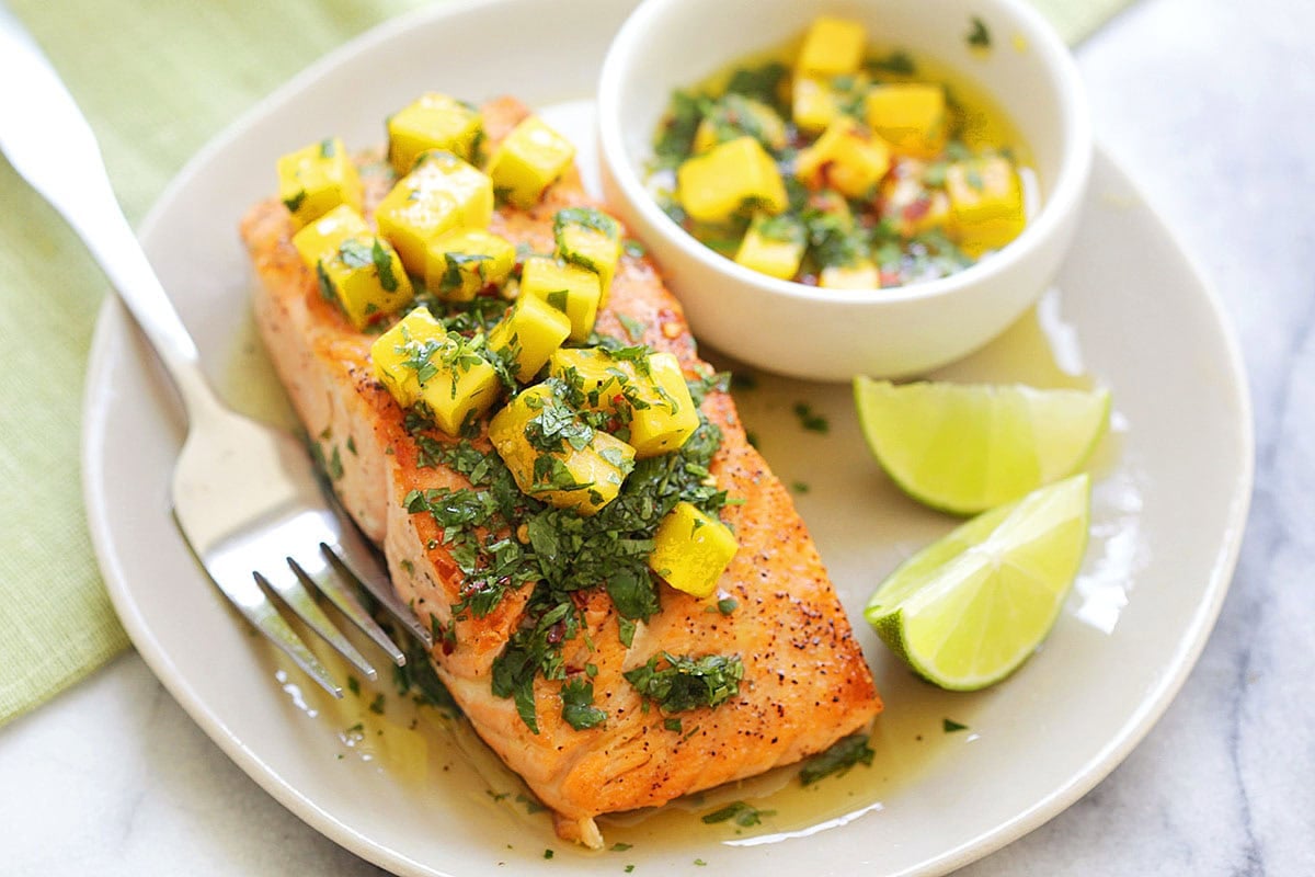 Juicy grilled salmon topped with sweet and tangy mango salsa, served with lime wedges and salsa in a small bowl