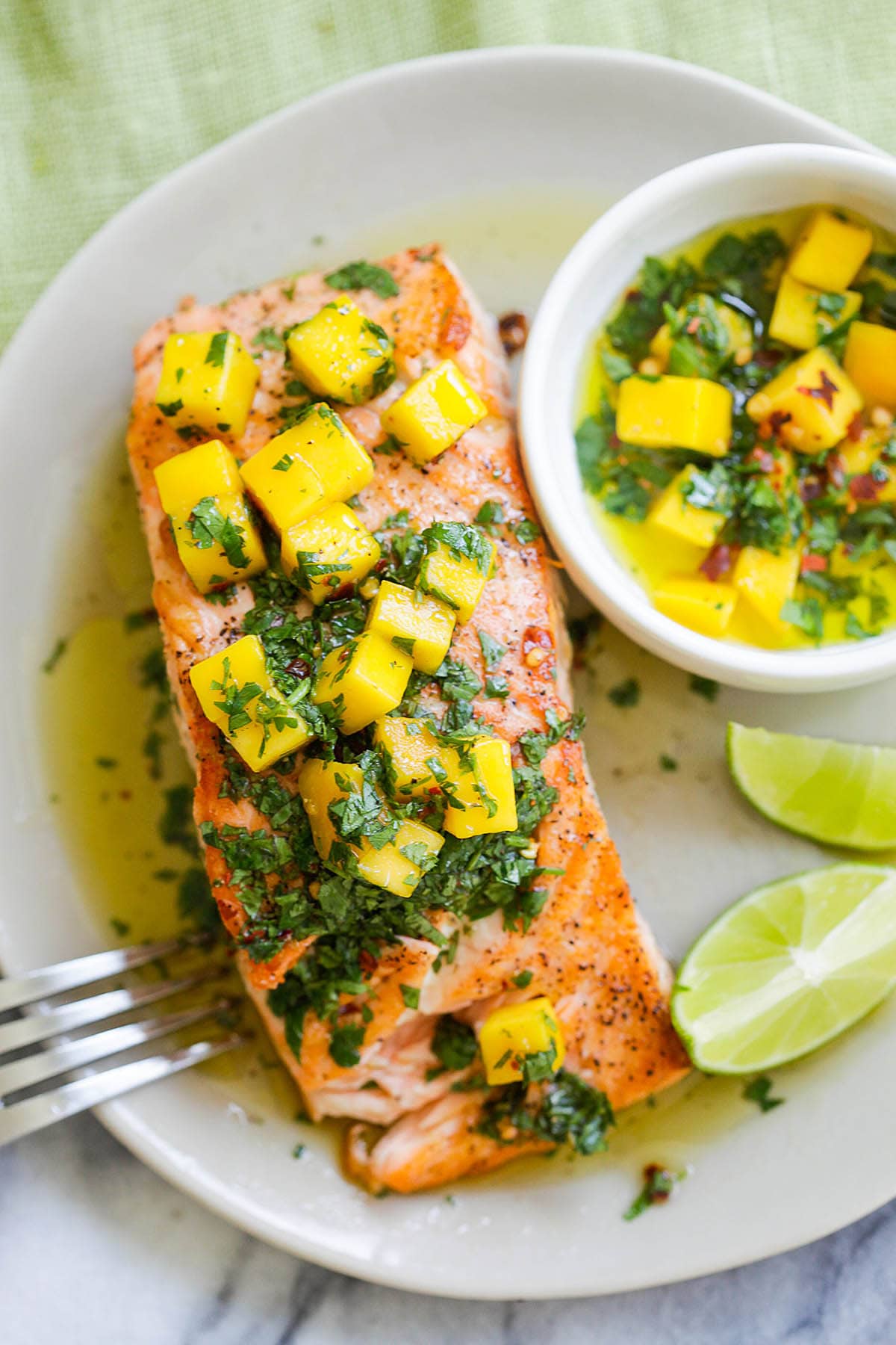 Salmon with mango salsa served with lime wedges and extra salsa in a bowl.