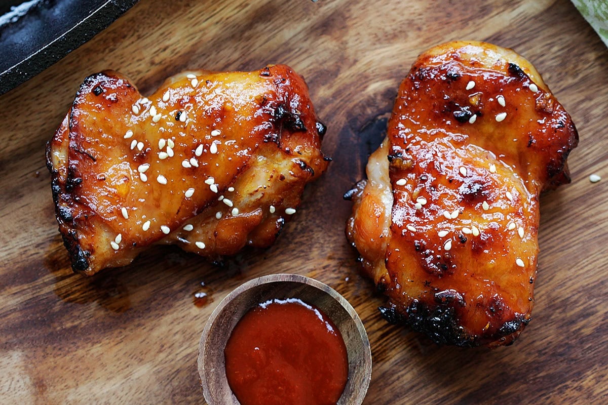 Glazed honey Sriracha chicken thighs on a chopping board.