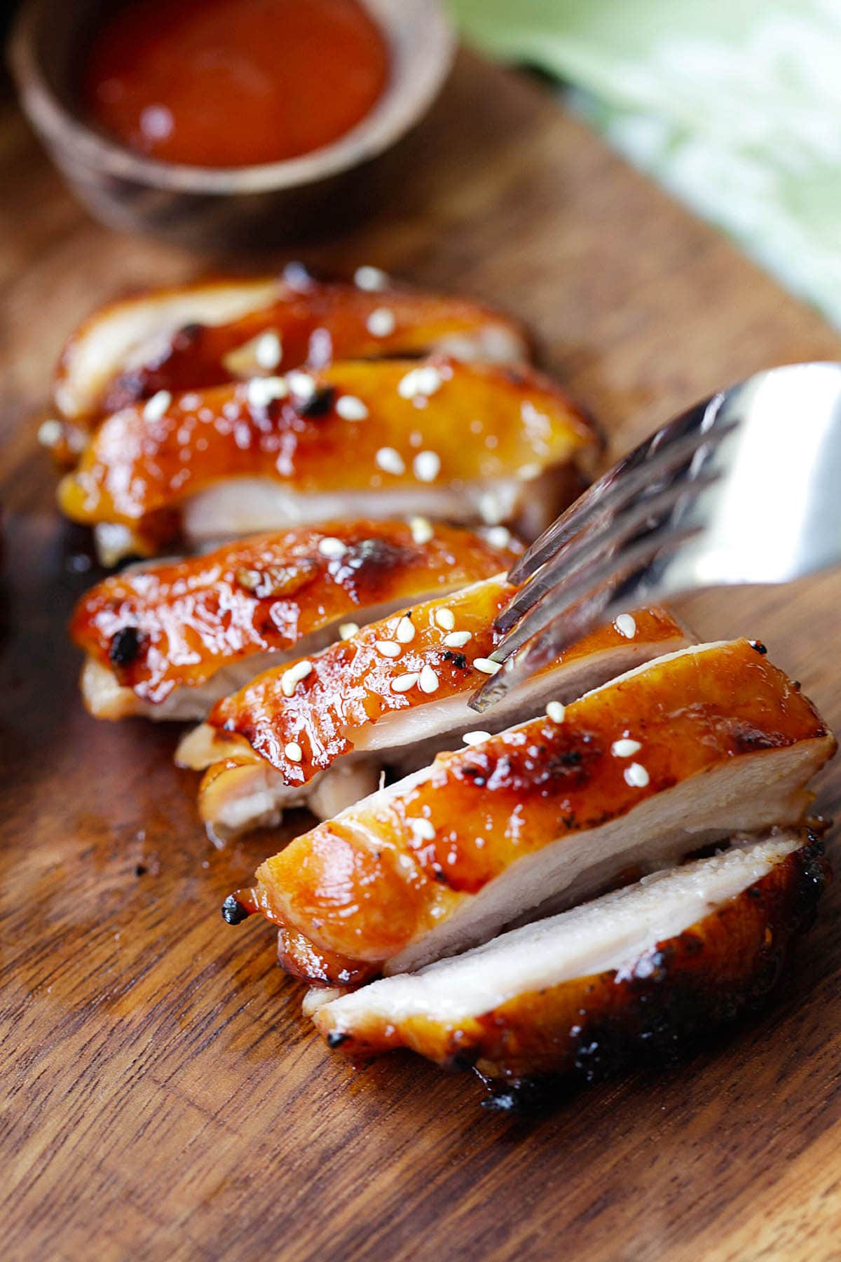 Sliced Sriracha chicken thigh, garnished with sesame seeds and pierced with a fork.