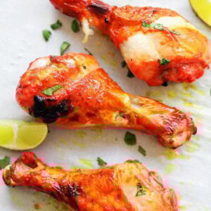 Oven baked tandoori chicken leg pieces on parchment paper, served with lime wedges.