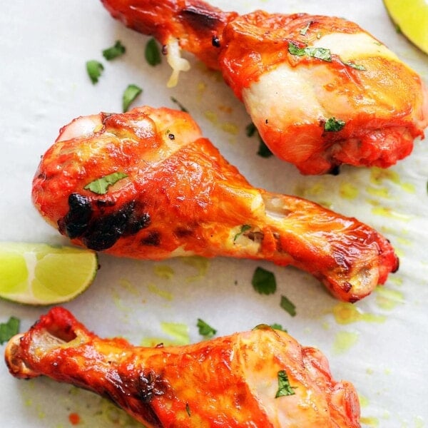 Oven baked tandoori chicken leg pieces on parchment paper, served with lime wedges.