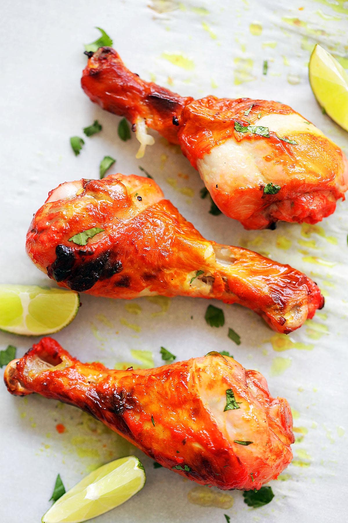 Oven baked tandoori chicken leg pieces on parchment paper, served with lime wedges.