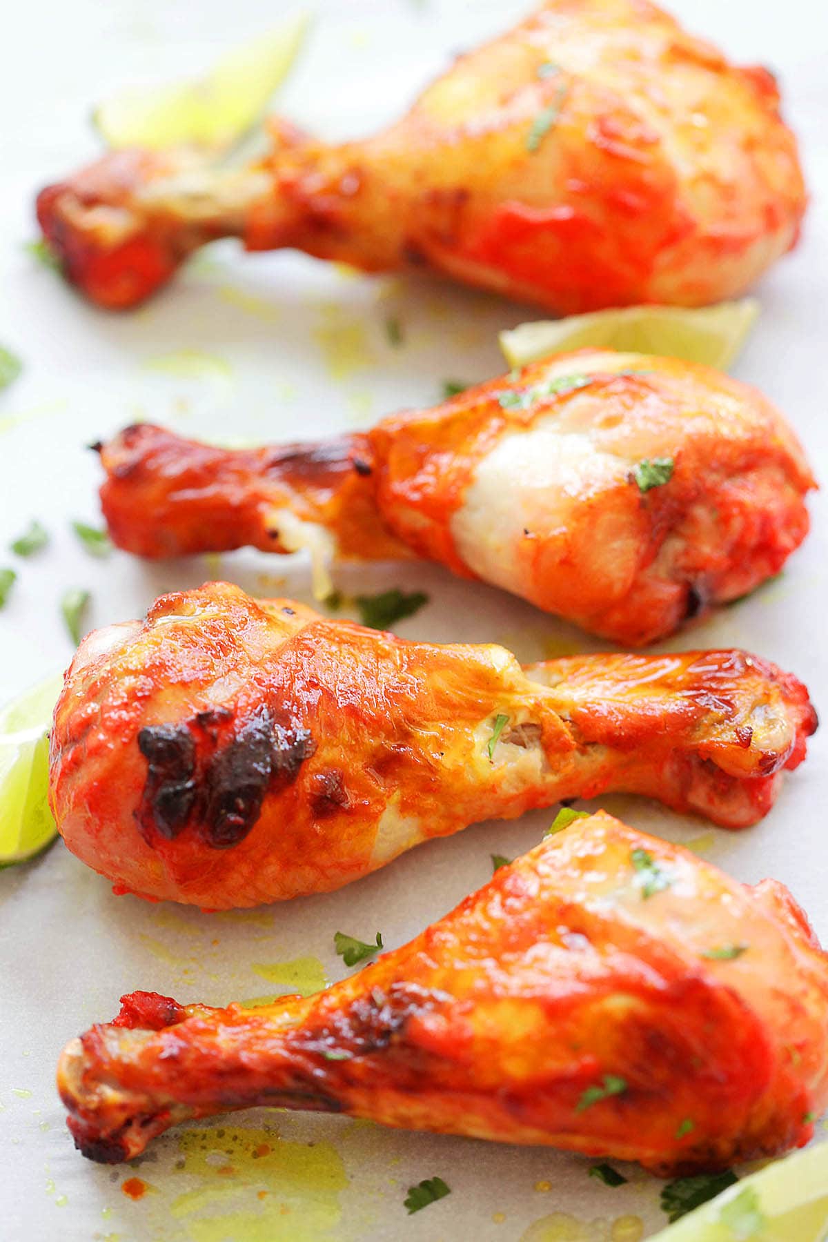 Homemade red tandoori chicken fresh from the oven, on parchment paper with lime wedges.