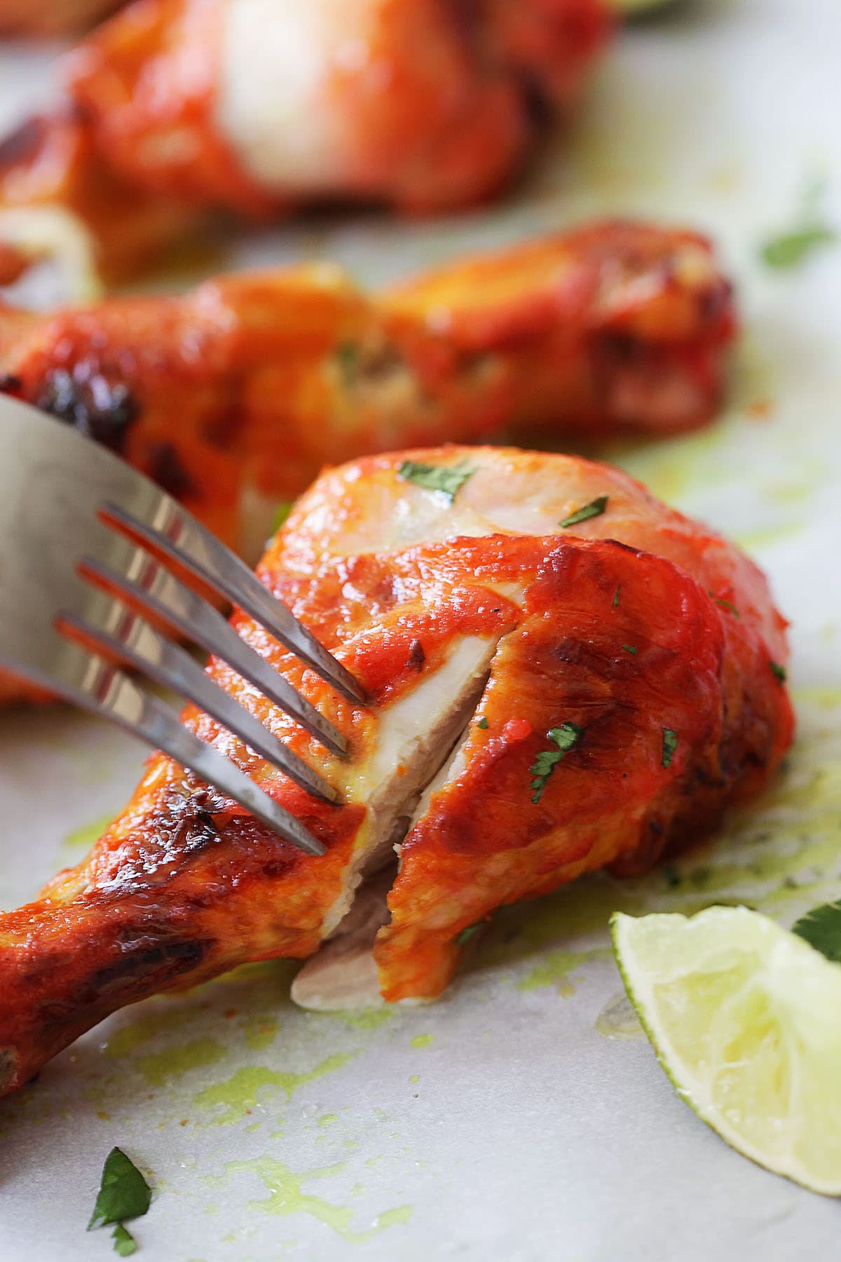 Tandoori chicken leg pierced with a fork, with charred red edges.