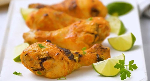 Juicy tandoori chicken leg pieces with a vibrant red color, arranged on parchment paper with lime.
