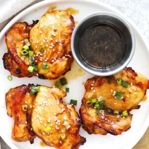 Air fryer teriyaki chicken recipe made with juicy boneless chicken thighs, garnished with sesame seeds and scallions on a plate.