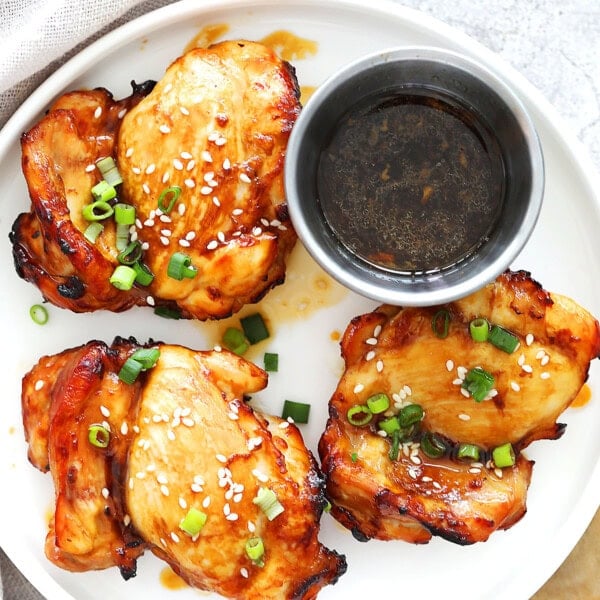 Air fryer teriyaki chicken recipe made with juicy boneless chicken thighs, garnished with sesame seeds and scallions on a plate.