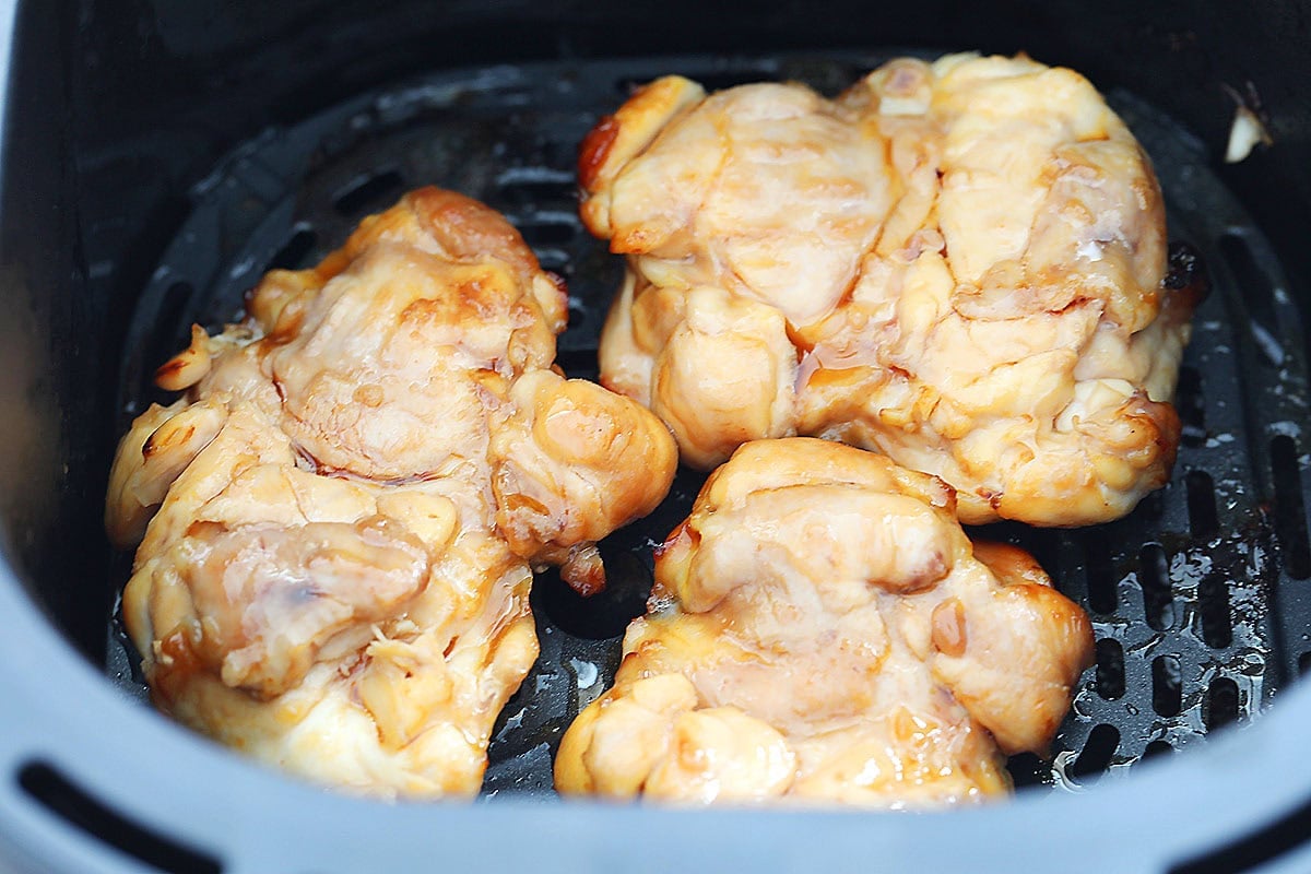 Marinated chicken thighs in an air fryer basket.