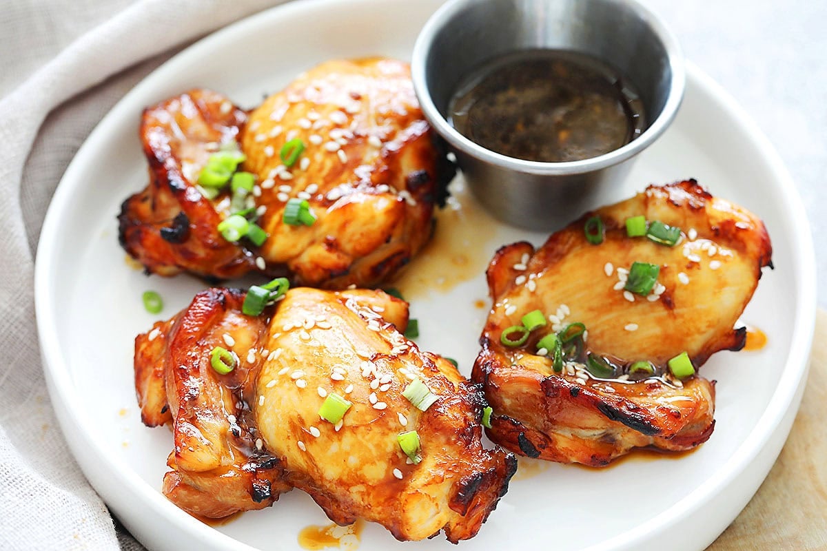Air fryer teriyaki chicken thighs served on a plate, garnished with sesame seeds and scallions.