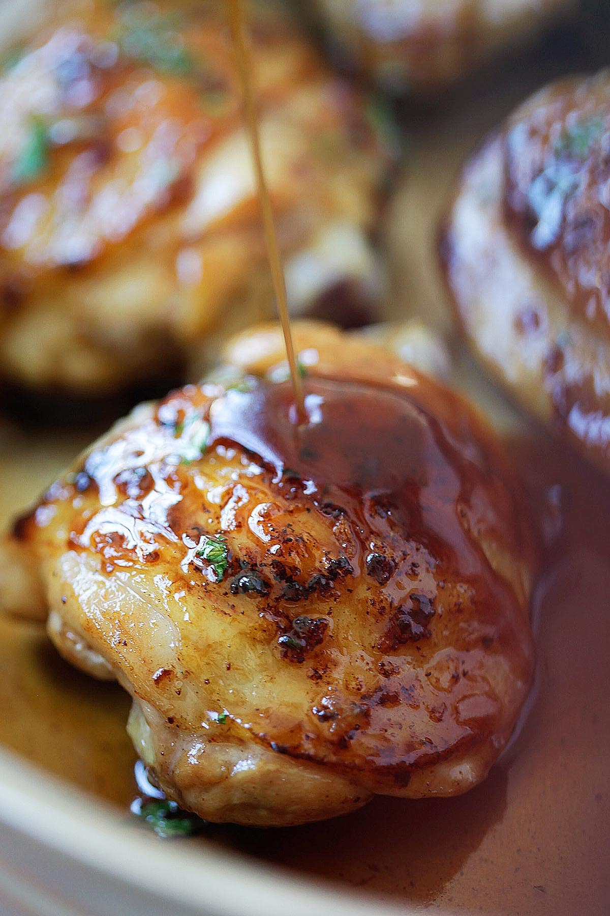Spoon drizzling glossy honey balsamic sauce over golden brown chicken thighs in a skillet.
