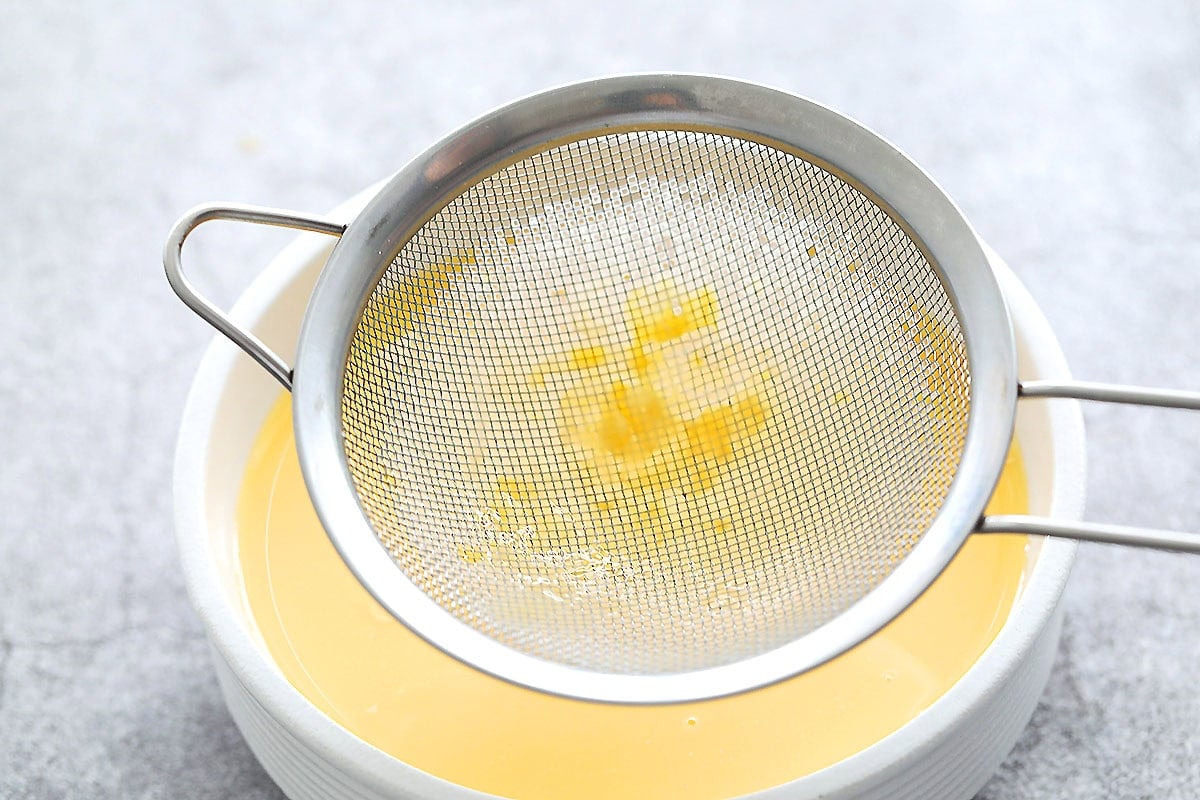 Strained egg mixture in a bowl with a fine mesh sieve on top, bits of egg left in the sieve.