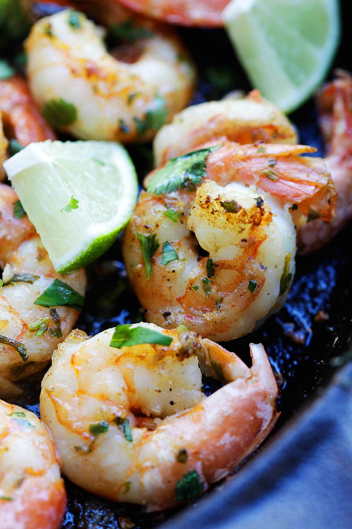 Garlic butter cilantro lime shrimp in a cast-iron pan, garnished with lime wedges for serving.
