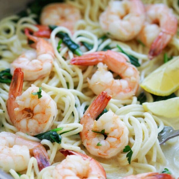 Garlic shrimp and spinach pasta served with lemon wedges.