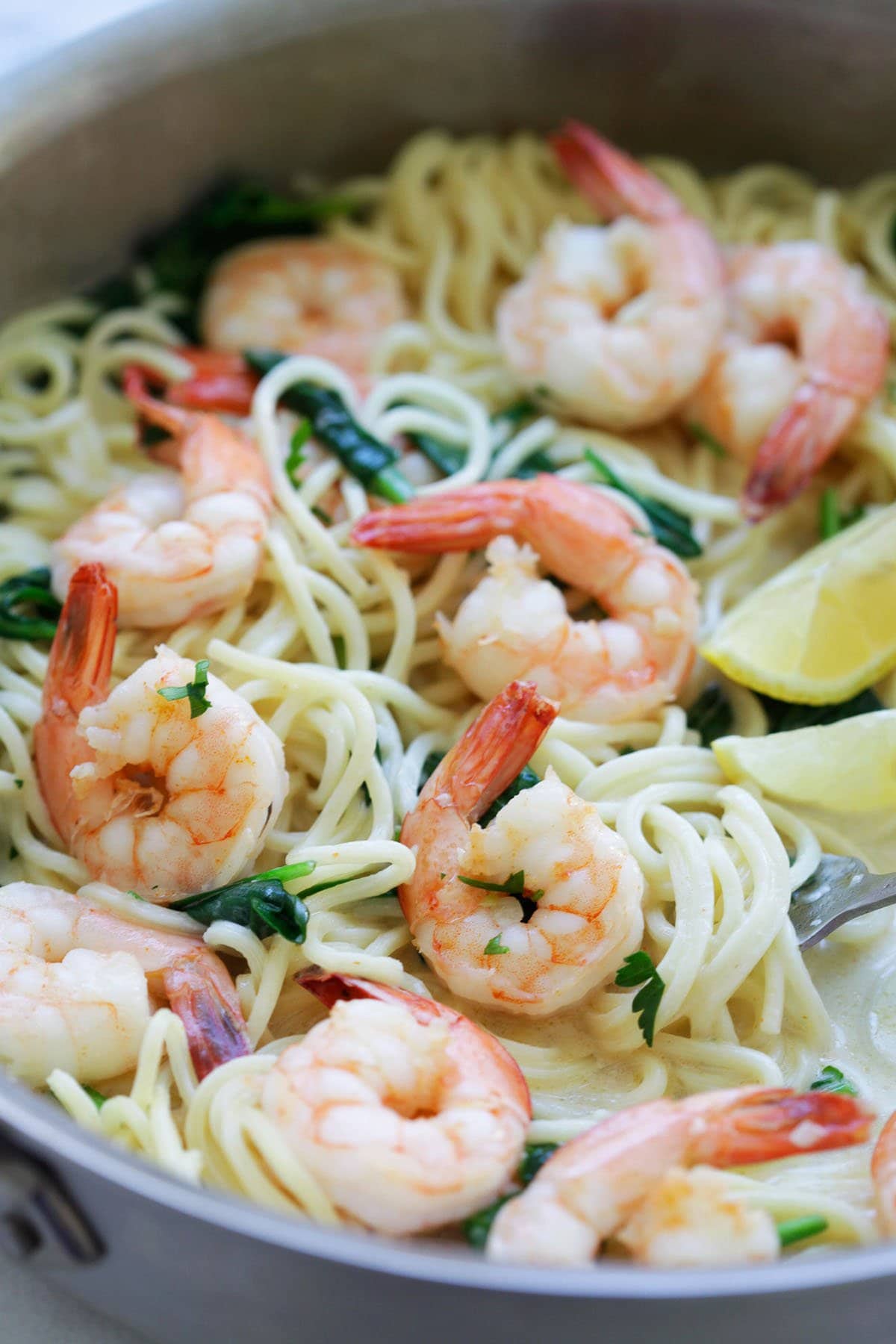 Garlic shrimp and spinach pasta served with lemon wedges.
