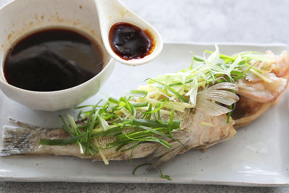 Homemade steamed fish sauce poured over steamed fish garnished with scallions and ginger.