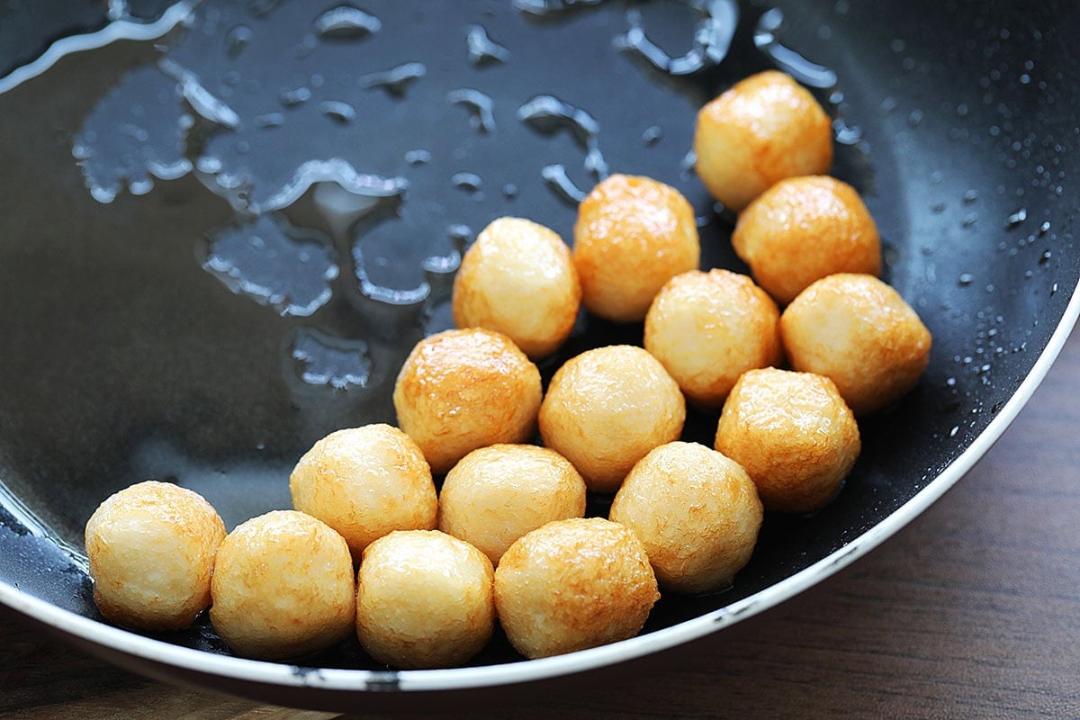 Golden pan-fried fish balls in a pan.
