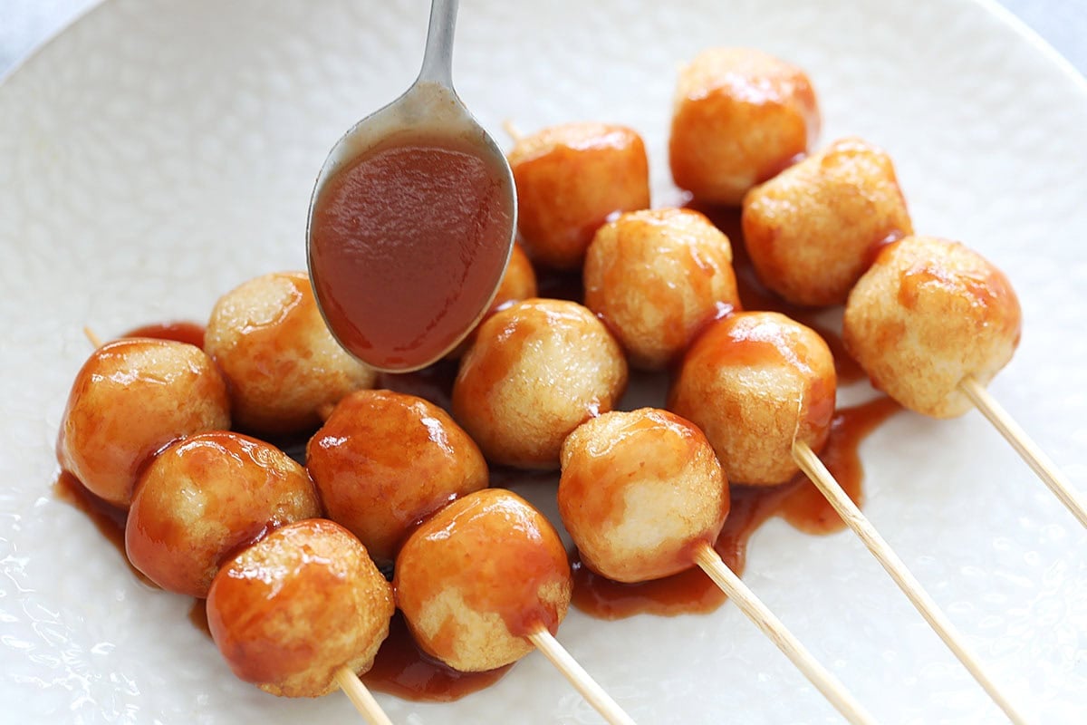 Pouring homemade sweet and sour sauce over skewered fish balls.