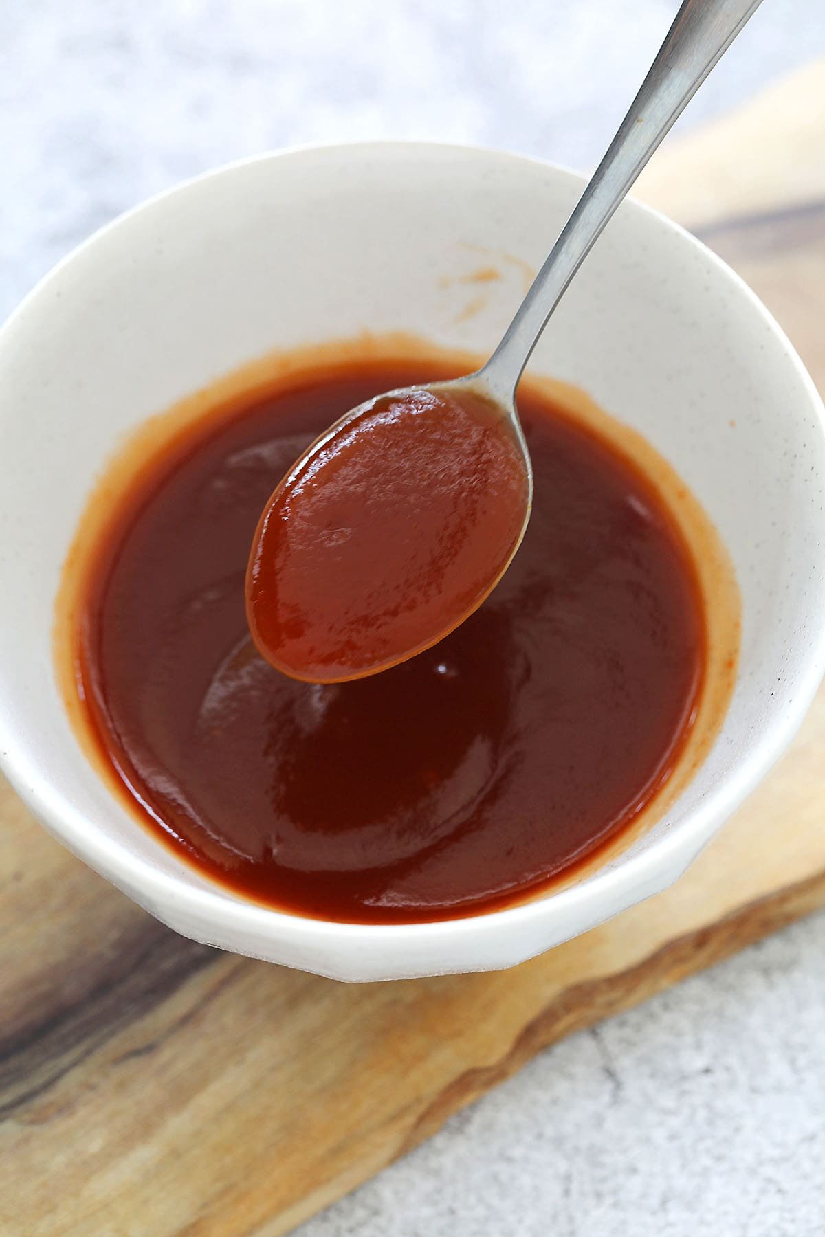 Spoonful of sweet and sour sauce held above a bowl.