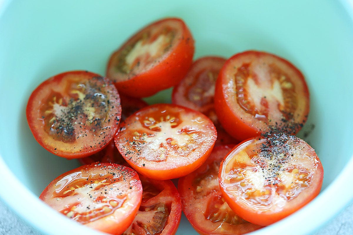 Tomatoes tossed with olive oil, salt and black pepper in a bowl.