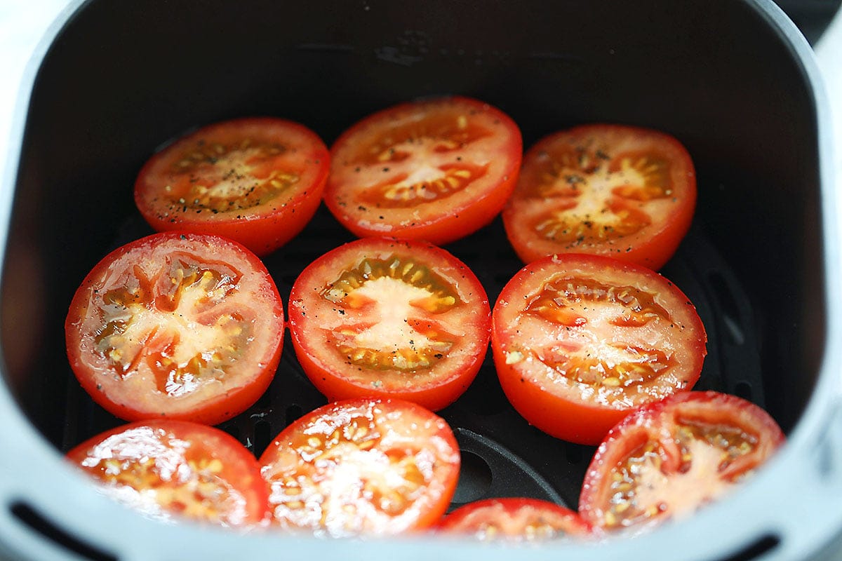Tomatoes arranged in a single layer in the air fryer basket.