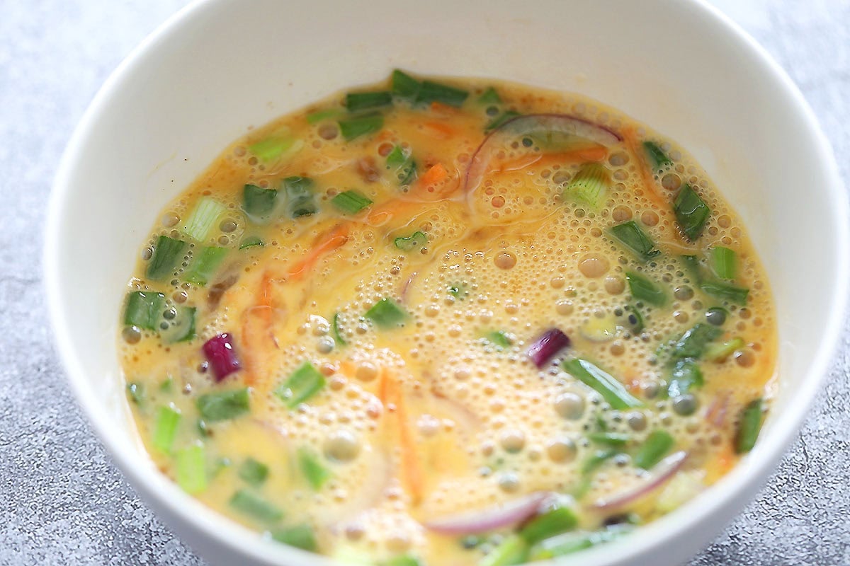 Egg mixture with onions, carrots, and scallions in a bowl.