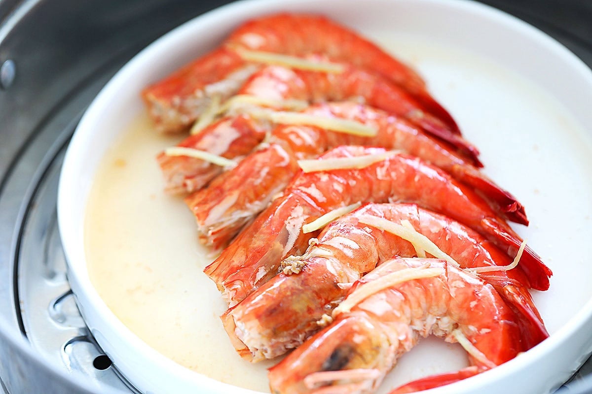 Cooked shrimp topped with ginger in a steamer.