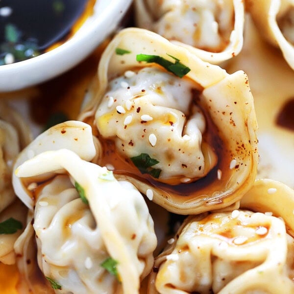 Szechuan red oil wontons garnished with sesame seeds.