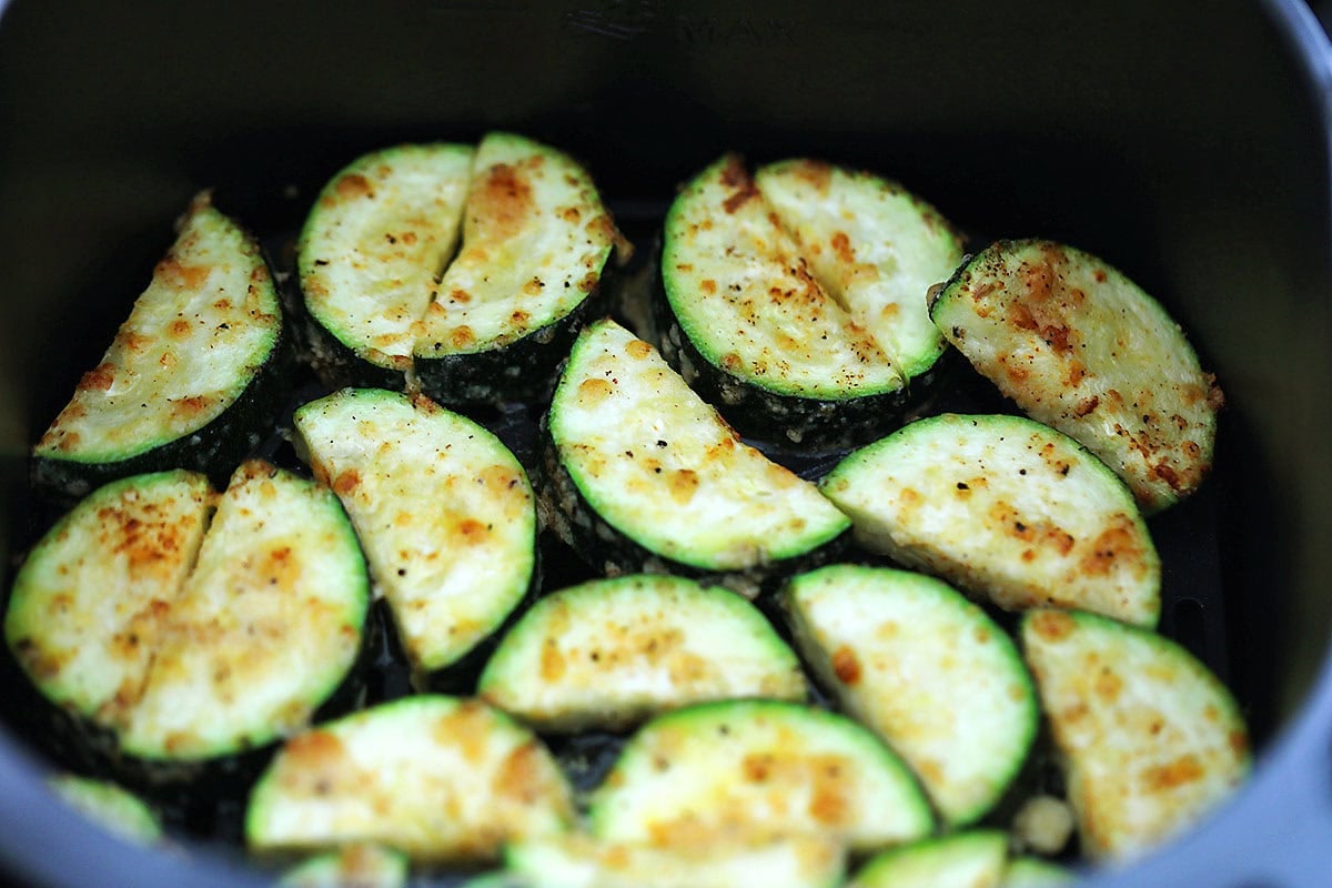 Golden brown zucchini slices in an air fryer basket.