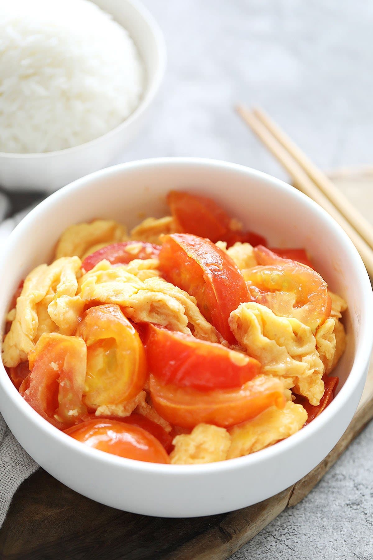 Chinese tomatoes and eggs served in a bowl, with a bowl of steamed white rice beside it.