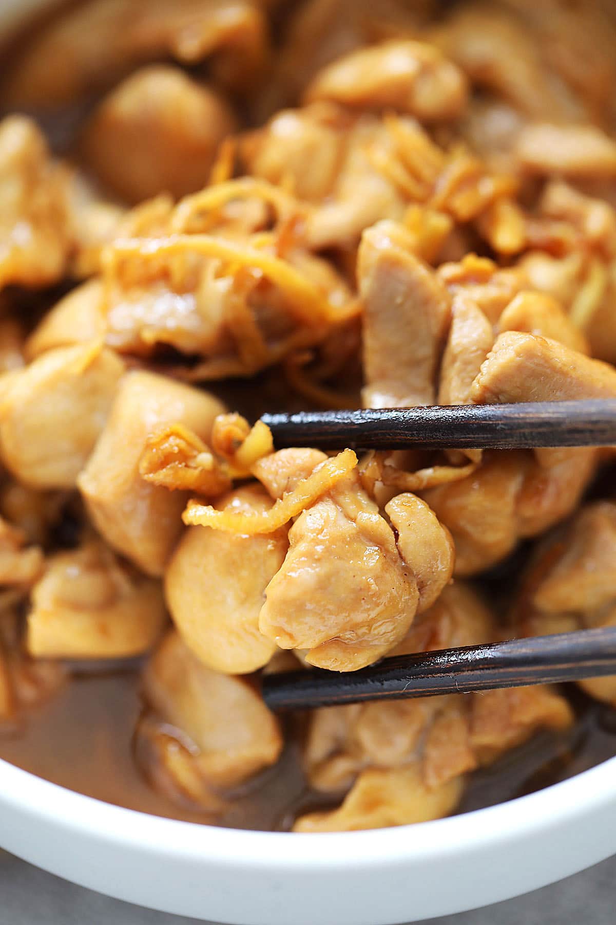 Juicy and tender sesame oil chicken and ginger strips picked up with a pair of chopsticks.