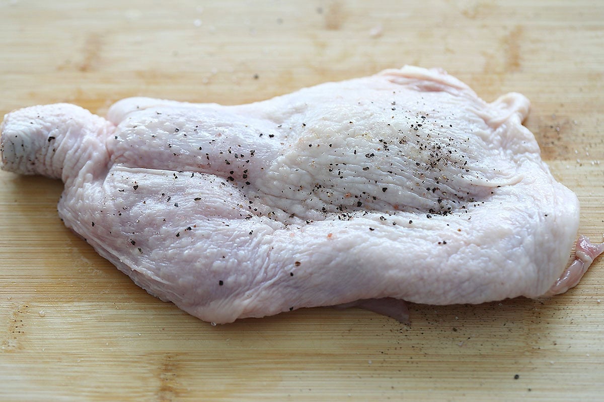 Seasoned chicken cutlet on a chopping board.