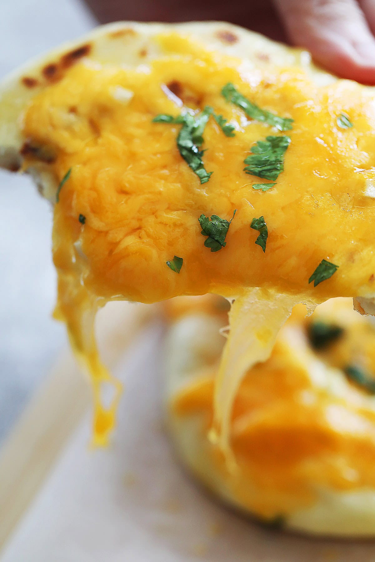 Cheesy garlic naan with melted cheddar on top, garnished with cilantro.