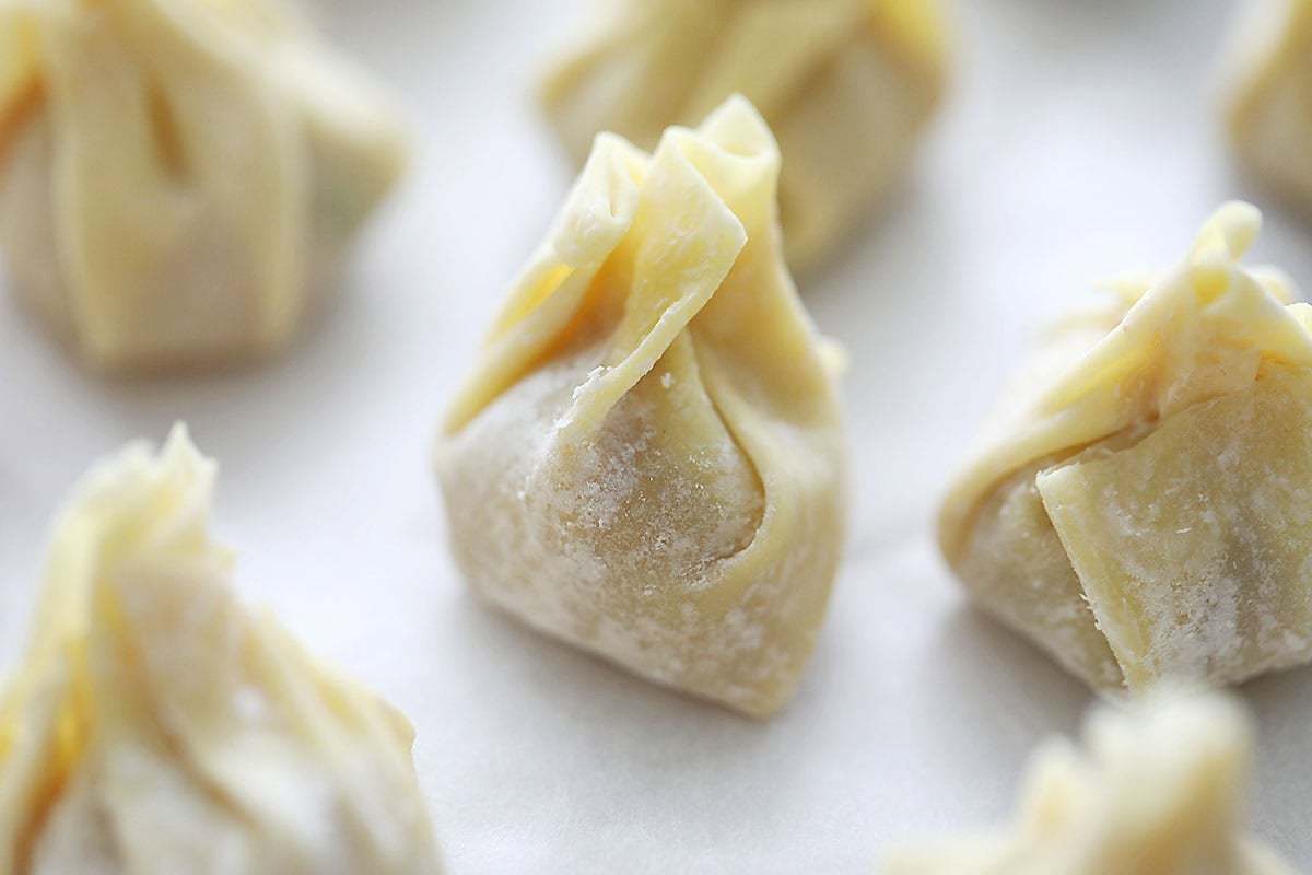 Raw chicken wontons on parchment paper.