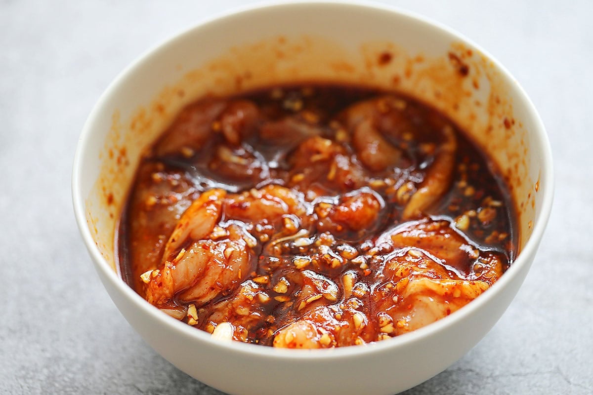 Chicken thighs with spicy gochujang marinade in a bowl.