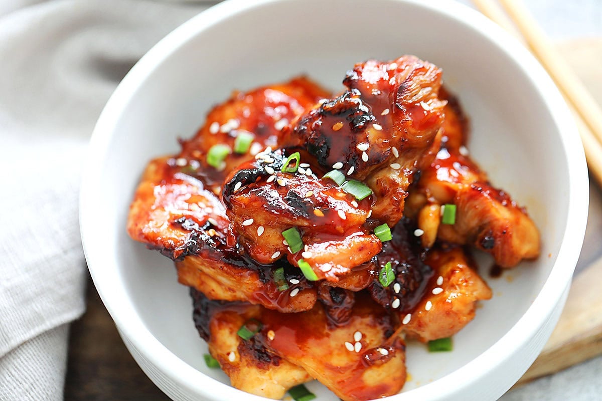 Slightly charred spicy Korean chicken garnished with sesame seeds and scallions.