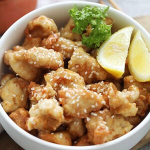 Lemon chicken garnished with white sesame seeds served in a bowl.