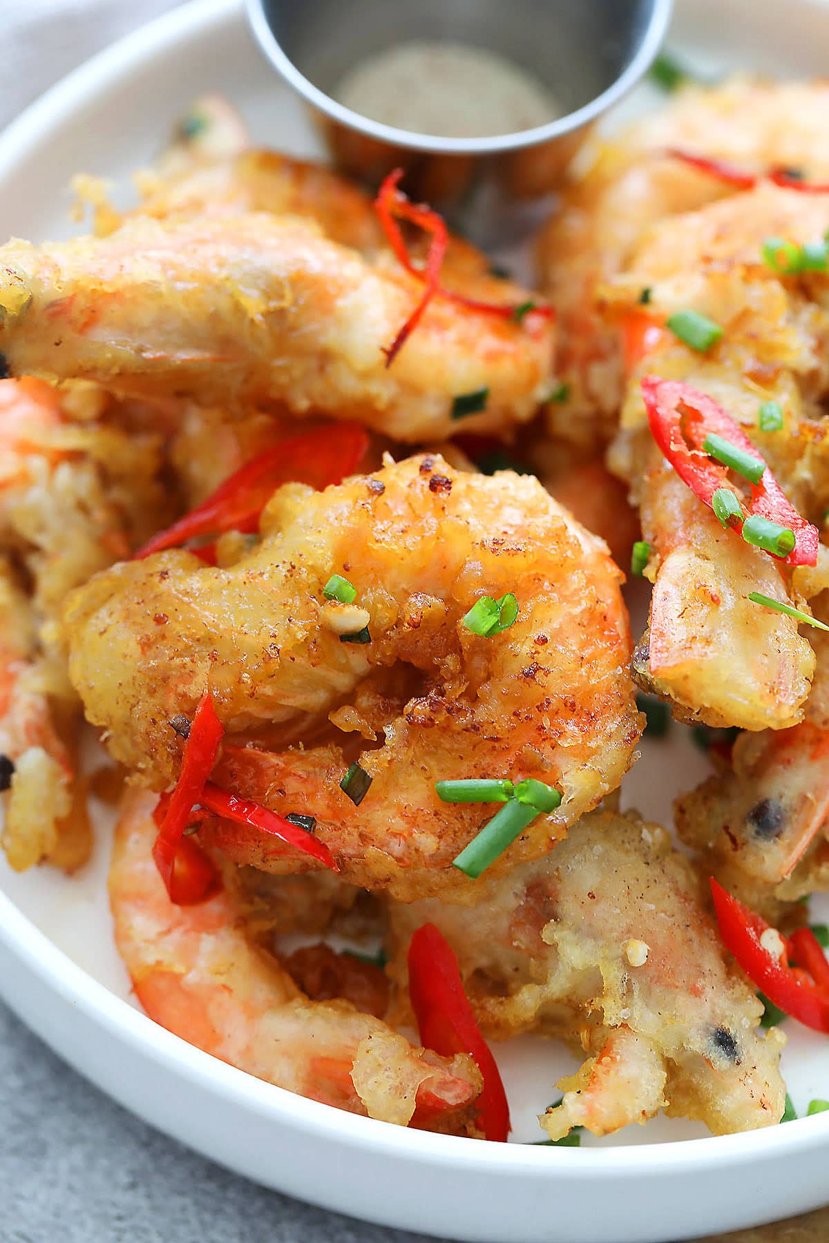 Salt and pepper shrimp with sliced chili and chopped scallions served on a plate.
