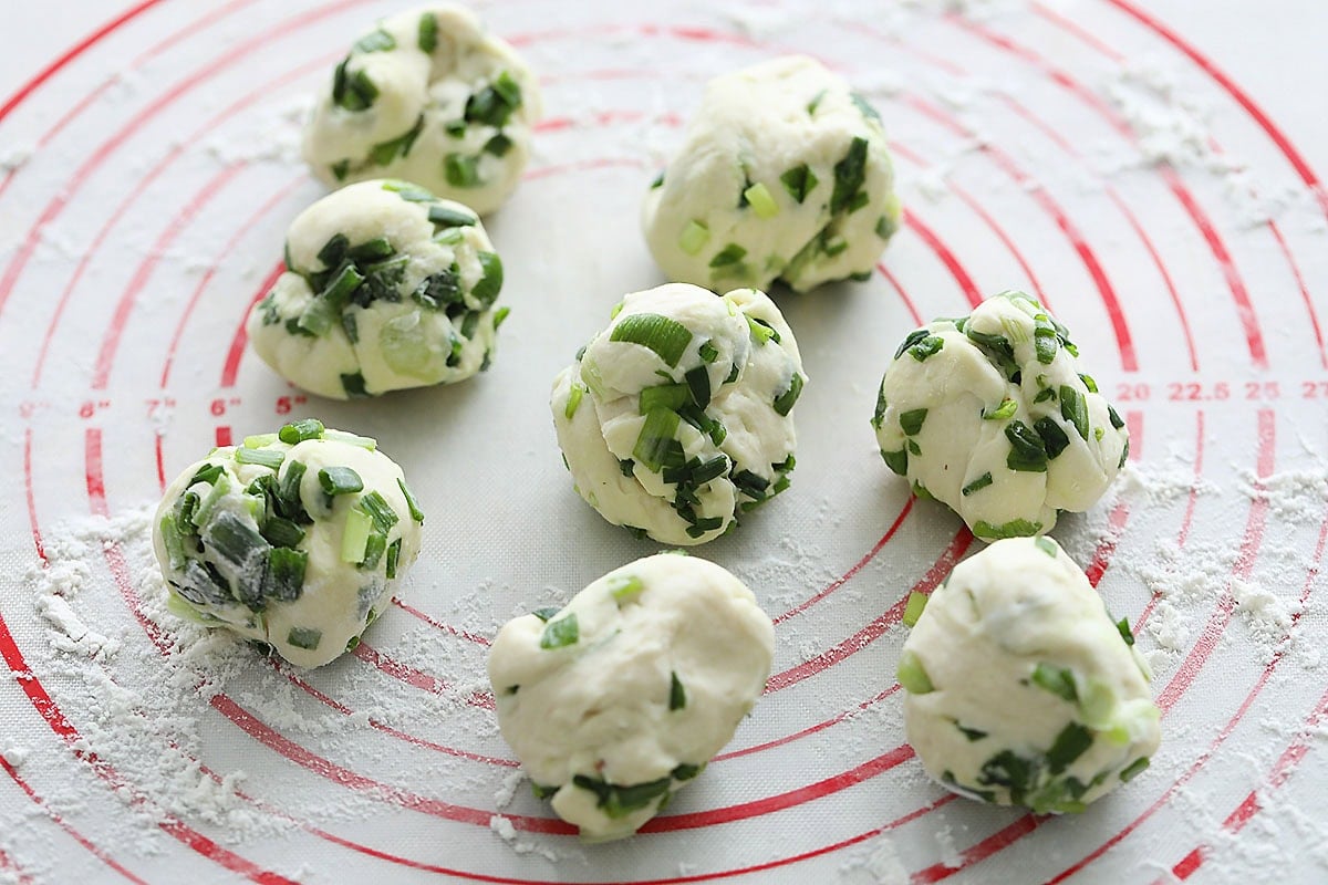 8 scallion dough balls on a silicon mat.