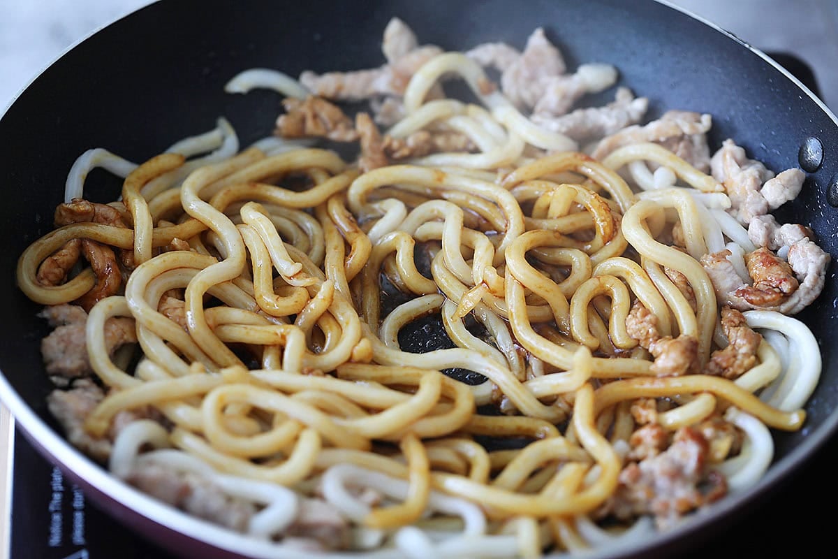 Pork, udon noodles and seasoning sauce in a skillet.